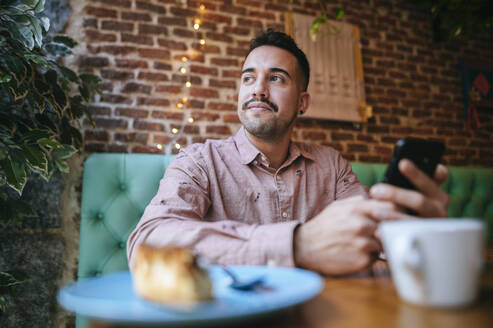 Porträt eines Mannes in einem Café, der ein Mobiltelefon hält - KIJF02943