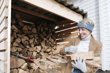 Porträt einer lächelnden reifen Frau, die Brennholz trägt - VYF00013