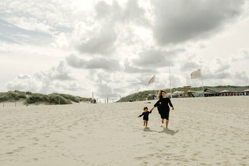 Mother and little daughter running hand in hand on the beach, The Hague, Netherlands - OGF00162