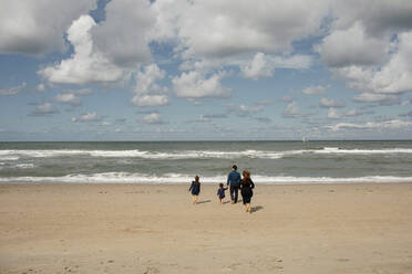 Rückenansicht einer Familie mit zwei Kindern, die barfuß am Strand laufen, Scheveningen, Niederlande - OGF00168