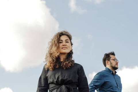 Porträt einer Frau vor dem Himmel mit ihrem Mann im Hintergrund, lizenzfreies Stockfoto