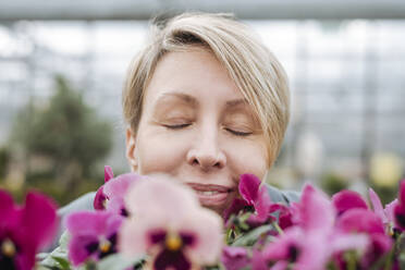 Lächelnde Frau riecht an Stiefmütterchen in einem Blumenladen - VYF00025