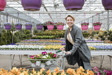 Smiling woman with pansies in shopping cart in flower shop - VYF00028