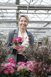 Germany, Wickede, happy woman with pink flowers pot in flower shop - VYF00036