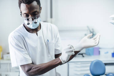 Porträt eines Zahnarztes mit Lupe und Maske, der in seiner Arztpraxis chirurgische Handschuhe anzieht - JCMF00388