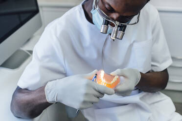 Zahnarzt mit Lupe und Maske bei der Arbeit an Zahnersatz in seiner Praxis - JCMF00390