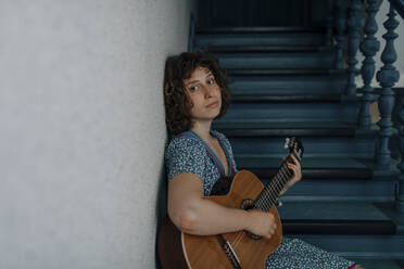 Porträt einer jungen Frau, die auf einer Treppe sitzt und Gitarre spielt - OGF00195