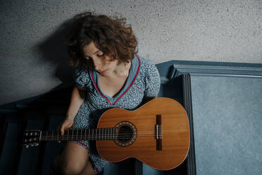 Traurige junge Frau sitzt mit Gitarre auf einer Treppe - OGF00204