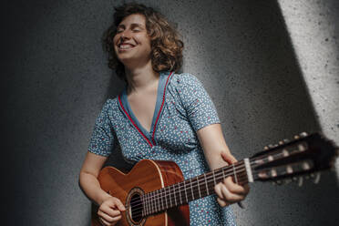 Porträt einer glücklichen jungen Frau, die mit geschlossenen Augen Gitarre spielt - OGF00207