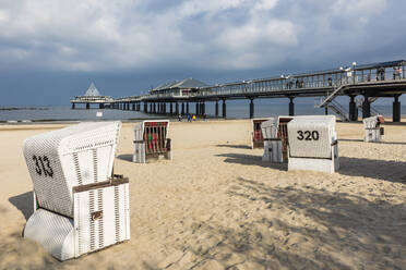Germany, Mecklenburg-Western Pomerania, Heringsdorf, Hooded beach chairs on sandy coastal beach with pier in background - WDF05851