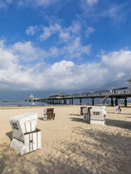 Germany, Mecklenburg-Western Pomerania, Heringsdorf, Clouds over hooded beach chairs on sandy coastal beach with pier in background - WDF05852