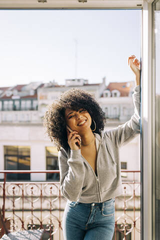 Portrait of happy young woman with curly hair on balcony on the phone stock photo