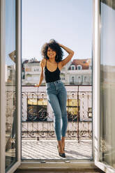 Porträt einer jungen Frau mit lockigem Haar auf einem Balkon stehend - DCRF00087