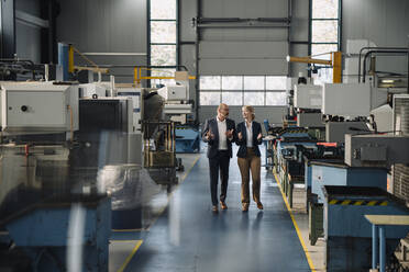 Businessman and businesswoman walking and talking in a factory - KNSF07681