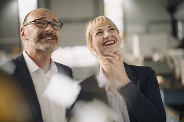 Portrait of happy businessman and businesswoman in a factory looking up - KNSF07687