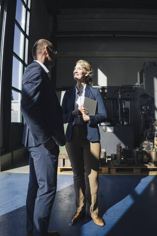 Businessman and smiling businesswoman talking in a factory stock photo