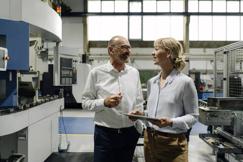 Mann und Frau mit Tablet im Gespräch in einer Fabrik - KNSF07704