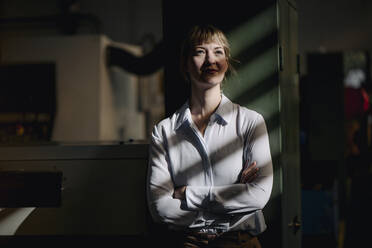 Porträt einer selbstbewussten Geschäftsfrau, die sich an einen Schrank in einer Fabrik lehnt - KNSF07705