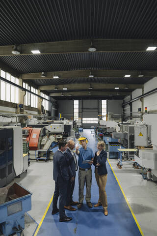 Geschäftsleute und Arbeiter mit Tablet im Gespräch in einer Fabrik, lizenzfreies Stockfoto
