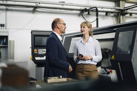 Businessman and woman with cell phone talking in a factory stock photo