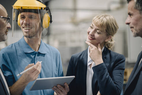 Business people and smiling worker with tablet talking in a factory - KNSF07748