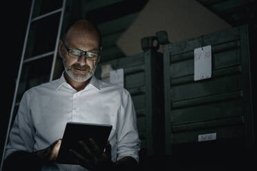 Businessman using tablet in a factory in the dark - KNSF07753