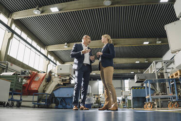 Businessman and businesswoman talking in a factory - KNSF07766