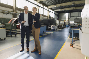 Confident businessman and businesswoman in a factory looking up - KNSF07769