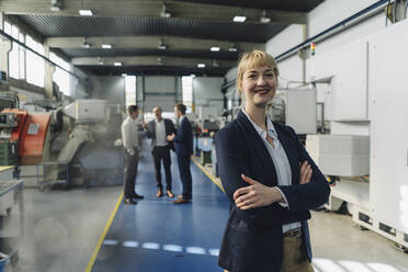 Portrait of a confident businesswoman in a factory with colleagues in backgound - KNSF07780