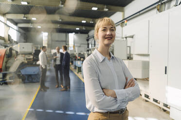 Portrait of a confident businesswoman in a factory with colleagues in backgound - KNSF07781