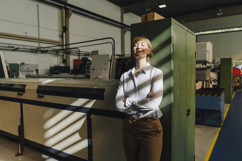 Businesswoman with closed eyes leaning against a cabinet in a factory stock photo