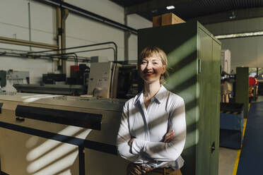 Porträt einer lächelnden Geschäftsfrau, die sich an einen Schrank in einer Fabrik lehnt - KNSF07786