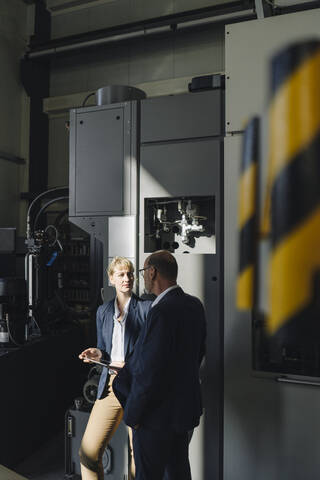 Geschäftsmann und Geschäftsfrau mit Tablet im Gespräch in einer Fabrik, lizenzfreies Stockfoto