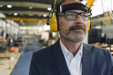 Portrait of a businessman wearing safety helmet and earmuffs in a factory - KNSF07807