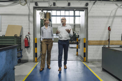 Mann und Frau gehen und sprechen in einer Fabrik, lizenzfreies Stockfoto