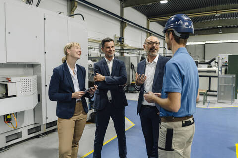Geschäftsleute und Arbeiter im Gespräch in einer Fabrik, lizenzfreies Stockfoto