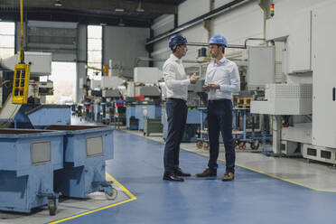 Two men wearing hard hats talking in a factory - KNSF07838
