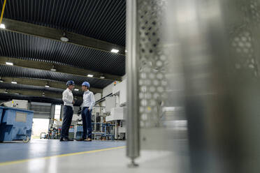 Two men wearing hard hats talking in a factory - KNSF07840