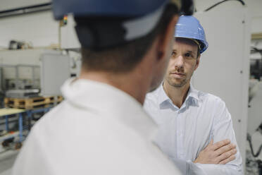 Zwei Männer mit Schutzhelmen unterhalten sich in einer Fabrik - KNSF07842