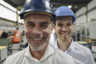 Porträt von zwei lächelnden Männern mit Schutzhelmen in einer Fabrik - KNSF07843