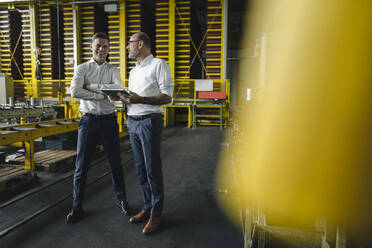 Zwei Geschäftsleute mit Tablet im Gespräch in einer Fabrik - KNSF07850