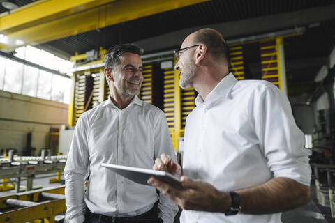 Zwei Geschäftsleute mit Tablet im Gespräch in einer Fabrik, lizenzfreies Stockfoto