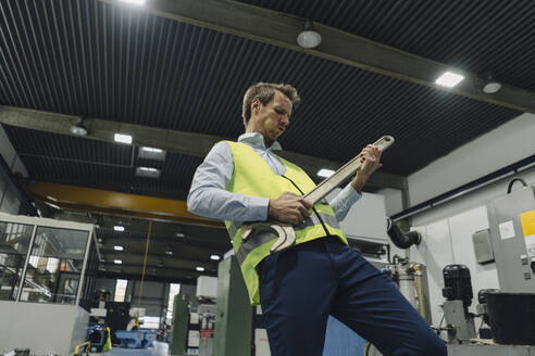 Mann mit reflektierender Weste in einer Fabrik spielt Luftgitarre auf großem Schraubenschlüssel - KNSF07868