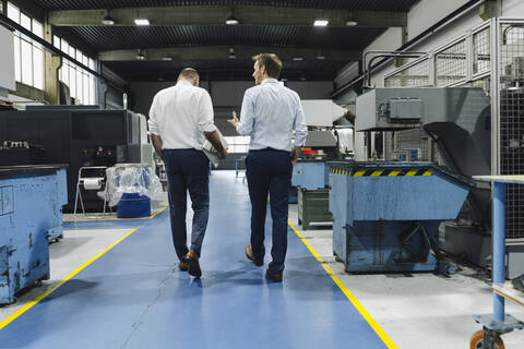 Rückansicht von zwei Männern, die sich in einer Fabrik unterhalten, lizenzfreies Stockfoto