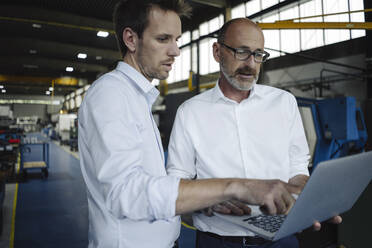 Two men using laptop in a factory - KNSF07880