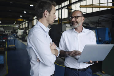 Two men using laptop in a factory - KNSF07881