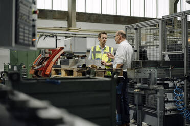 Geschäftsmann und Mann mit reflektierender Weste unterhalten sich in einer Fabrik - KNSF07886