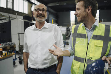 Businessman and man in reflective vest talking in a factory - KNSF07889