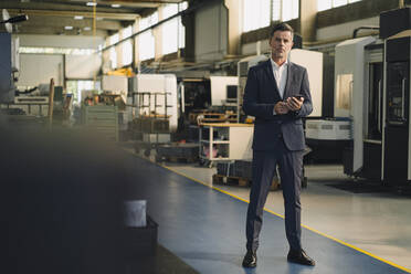 Portrait of a businessman with cell phone in a factory - KNSF07897