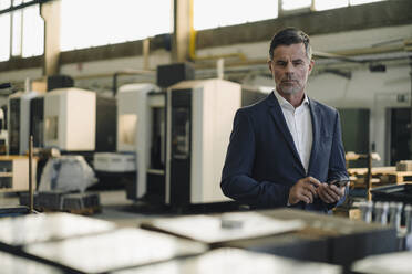 Portrait of a businessman with cell phone in a factory - KNSF07899